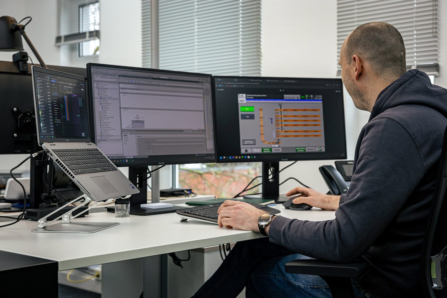 Mann arbeitet an mehreren Monitoren mit Automatisierungssoftware und Fördertechnik-Programmierung im modernen Büro