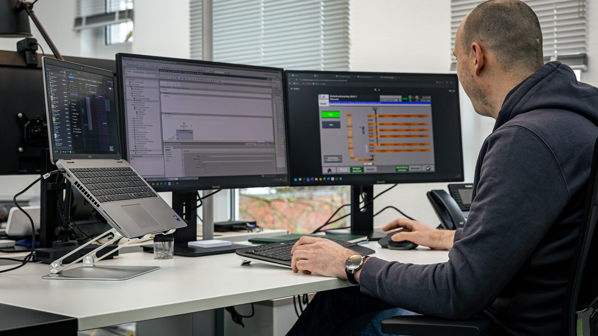 Mann arbeitet an mehreren Monitoren mit Automatisierungssoftware und Fördertechnik-Programmierung im modernen Büro