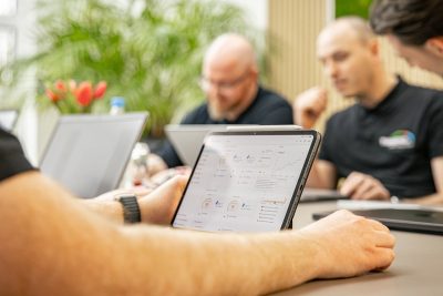 Geschäftsteam arbeitet gemeinsam an Tablets und Laptops in modernem Büro mit Pflanzen im Hintergrund