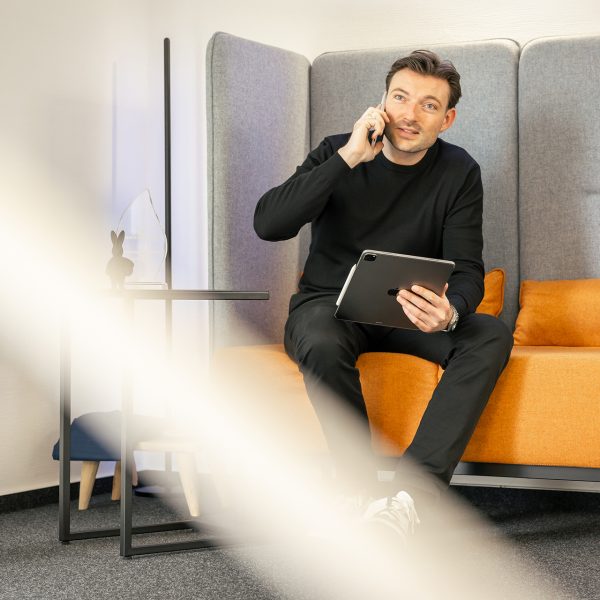 Geschäftsmann telefoniert mit Tablet auf orange-grauem Sessel in modernem Büro