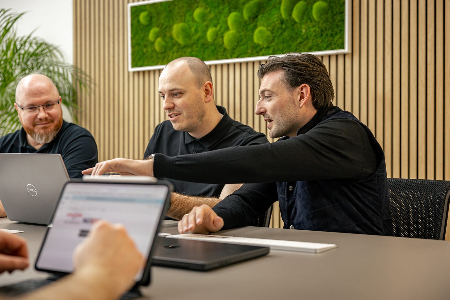 Drei Männer in schwarzer Kleidung arbeiten gemeinsam an Laptops in einem modernen Büro mit Holzwänden