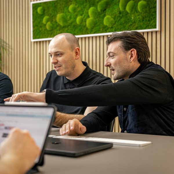 Drei Männer in schwarzer Kleidung arbeiten gemeinsam an Laptops in einem modernen Büro mit Holzwänden