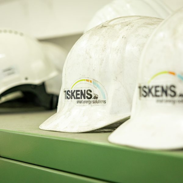 Weiße Bauhelme mit TISKENS Logo und Schriftzug "smart energy solutions" auf grünem Schreibtisch im Büro