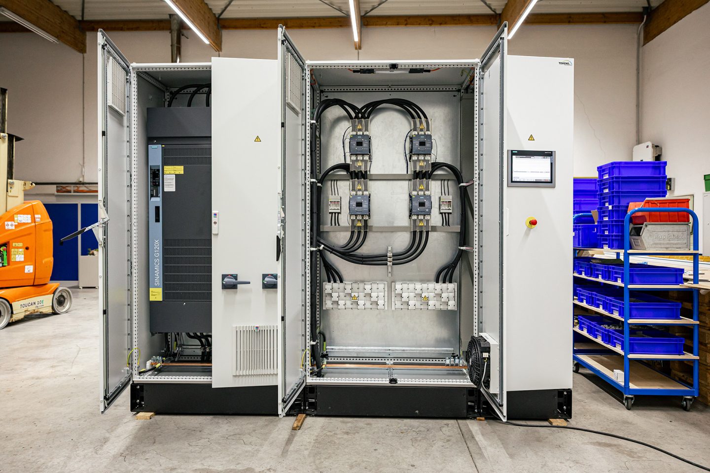 Industrieller Antriebsschrank mit geöffneten Türen zeigt elektrische Komponenten und Kabelführung in Produktionshalle