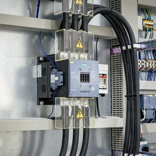 Industrieller Schaltschrank mit Leistungsschalter, Kabeln und Warnhinweisen für elektrische Automatisierungstechnik