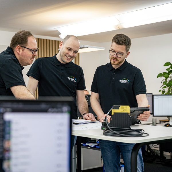Drei Kollegen in schwarzen Poloshirts analysieren gemeinsam Energiedaten an einem Tablet im modernen Büro