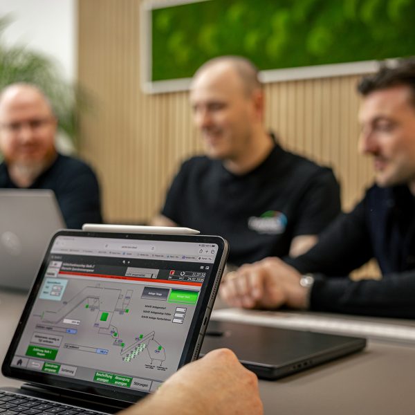 Drei Männer in schwarzer Kleidung betrachten Energiemanagement-Software auf Laptop-Bildschirm in modernem Büro