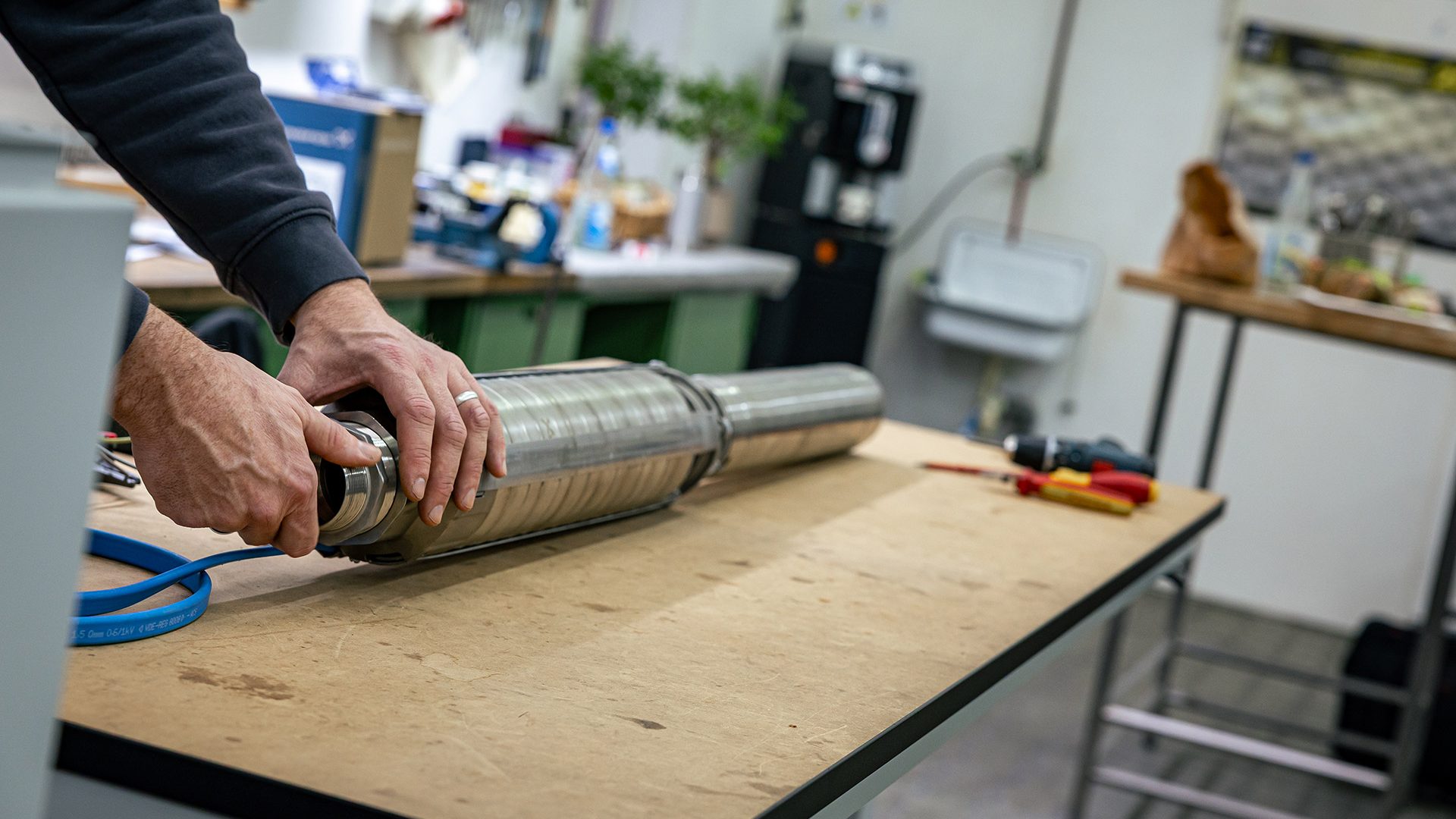 Mann installiert Lüftungsrohr aus Metall auf Holzarbeitsfläche in heller Werkstatt mit Werkzeugen