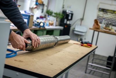 Mann installiert Lüftungsrohr aus Metall auf Holzarbeitsfläche in heller Werkstatt mit Werkzeugen