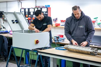 Zwei Techniker warten eine Pumpe in der Werkstatt - einer bedient Prüfgerät, der andere montiert Pumpenkomponenten