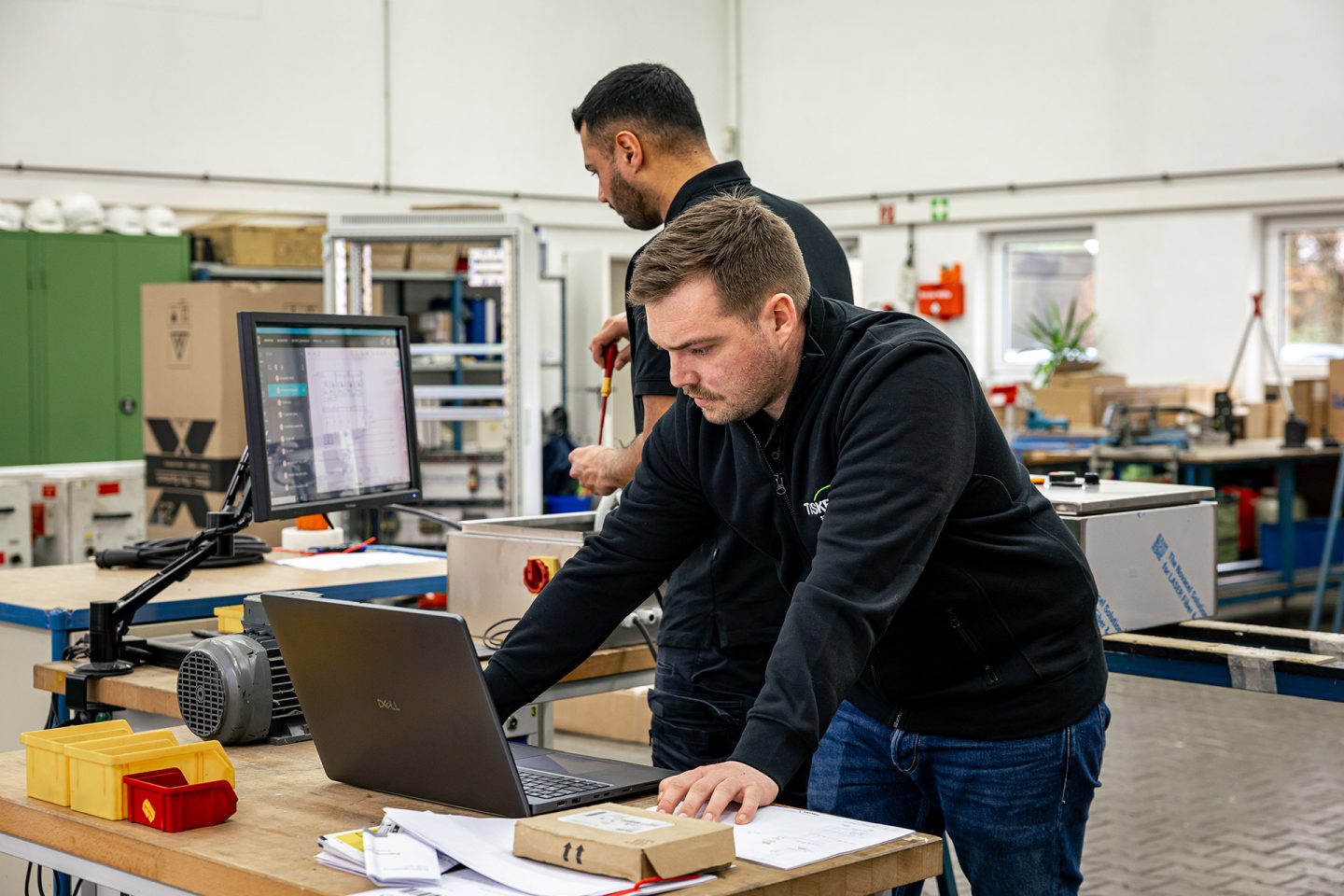 Zwei Techniker arbeiten gemeinsam am Laptop in einer Werkstatt bei der Modernisierung von Industrieanlagen