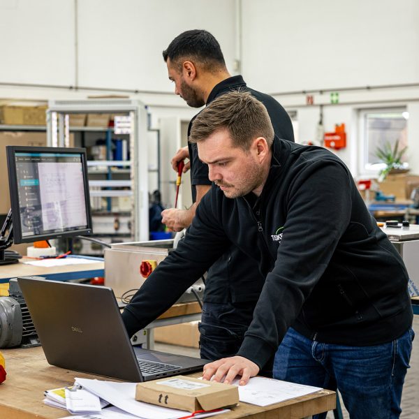 Zwei Techniker arbeiten gemeinsam am Laptop in einer Werkstatt bei der Modernisierung von Industrieanlagen