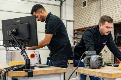 Zwei Techniker arbeiten an Werkbank mit Computer und Elektromotor in industrieller Werkstatt für Retrofit-Modernisierung