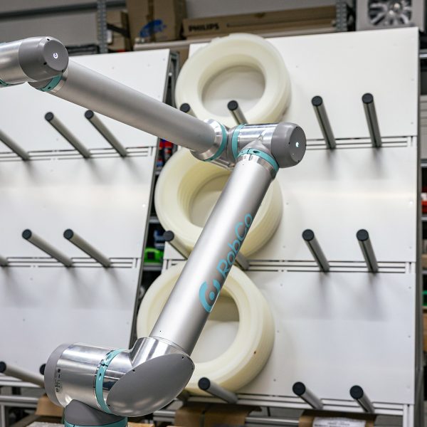 Silberner Roboterarm mit türkisen Akzenten vor weißer Werkstattwand in technischer Arbeitsumgebung