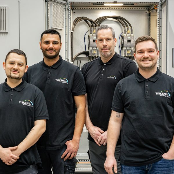 Vier Servicetechniker in schwarzen Poloshirts stehen vor einer Industrieanlage in einer Werkstatt