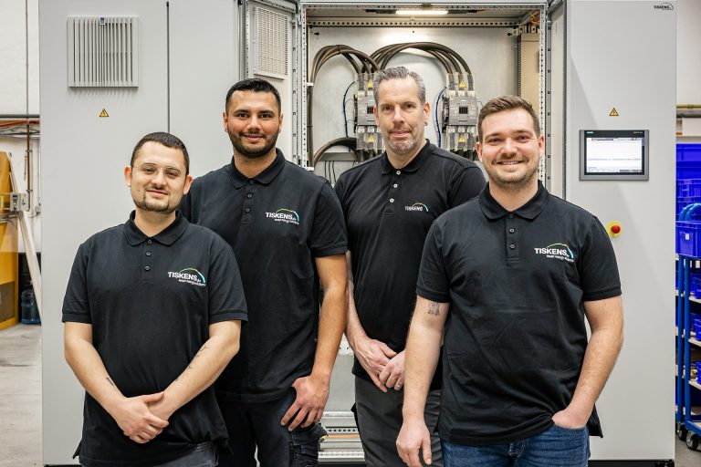 Vier Servicetechniker in schwarzen Poloshirts stehen vor einer Industrieanlage in einer Werkstatt