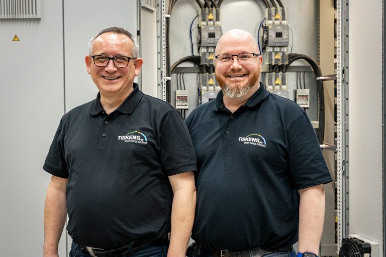 Zwei Techniker in TISKENS-Poloshirts vor elektrischen Schaltanlagen im Servicezentrum